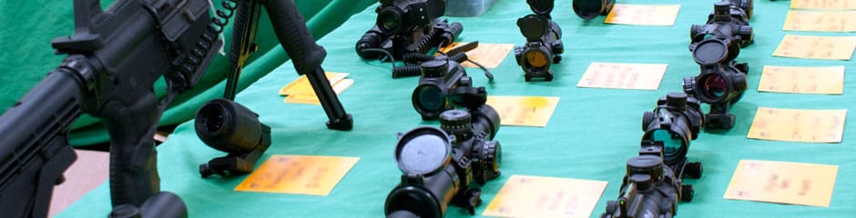 Rifle and scopes displayed on trade show table.
